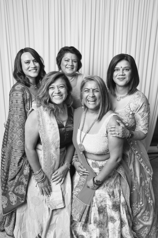 Five women in saris stand together smiling