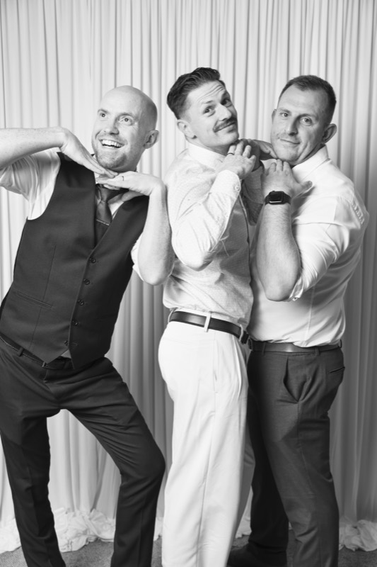 Three men in shirts strike a playful boy band pose
