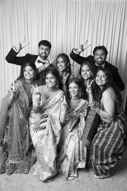 A big group of friends in saris and suits throw up peace signs